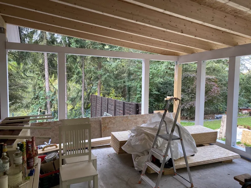 Innenansicht der überdachten Terrasse mit sichtbarer Holzbalkendecke und Blick in den Garten