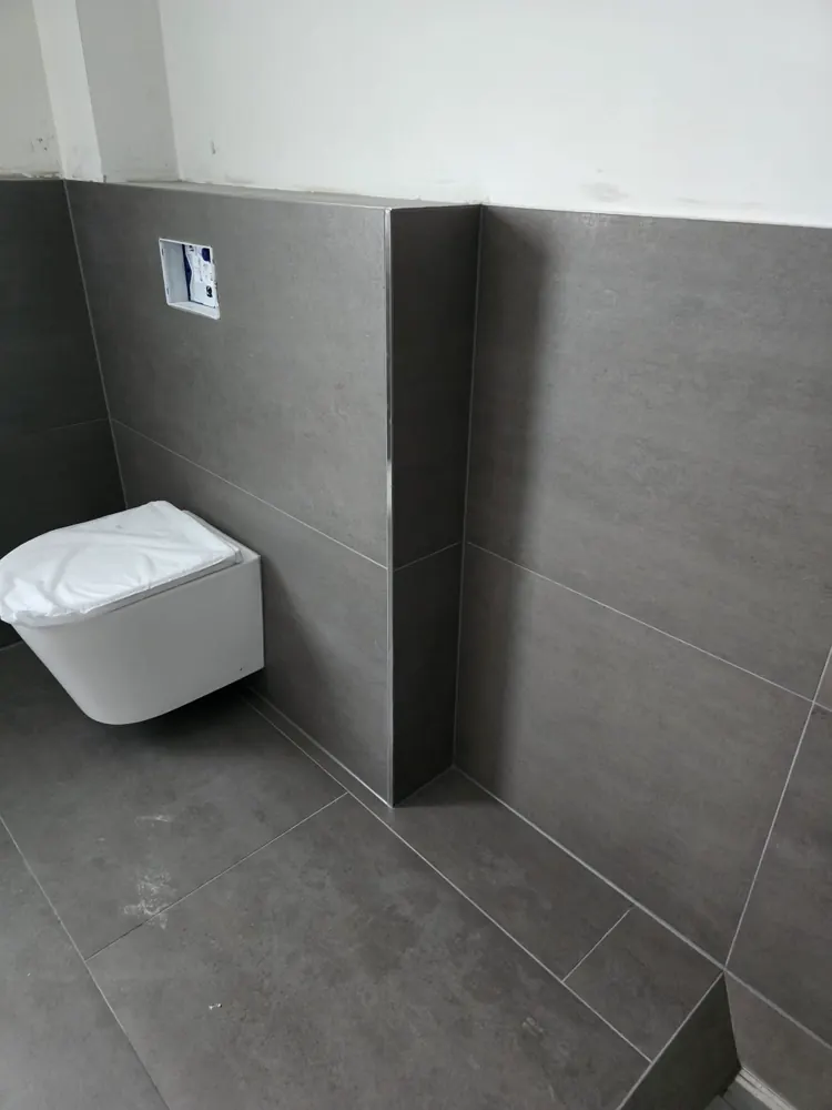 Wand-WC vor großformatigen grauen Fliesen mit Vorwandinstallation und Eckschiene