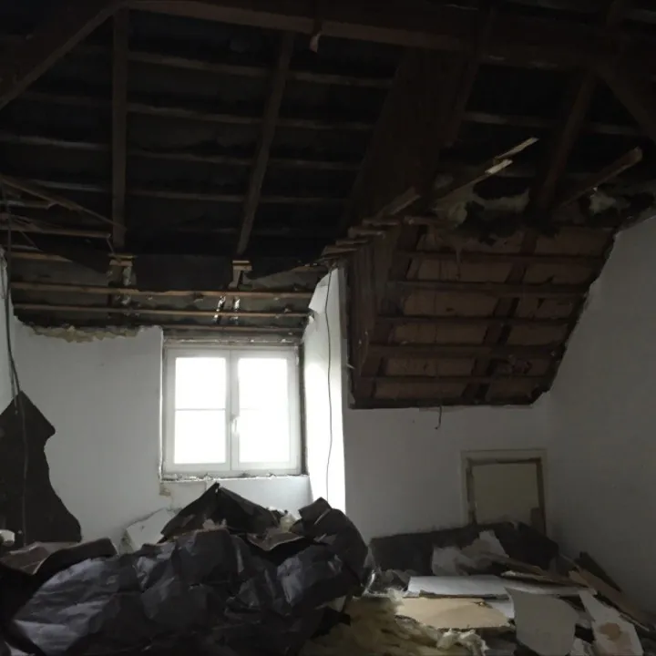 Entkerntes Zimmer unter der Dachschräge mit abgerissener Deckenverkleidung