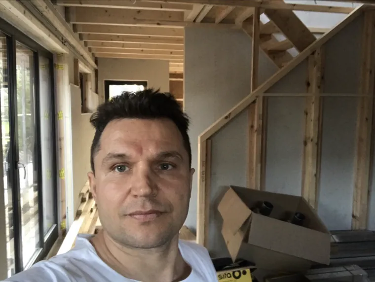 Oleg Prusincov auf einer Baustelle vor einem Ständerwerk aus Holz mit beplankten Wänden