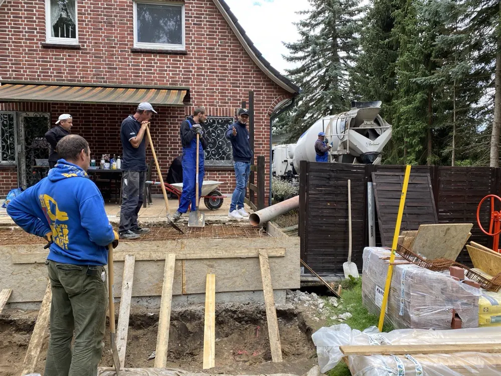 Bewehrung in der Schalung vor dem Betonieren, Mischfahrzeug und Bauteam an der Hauswand