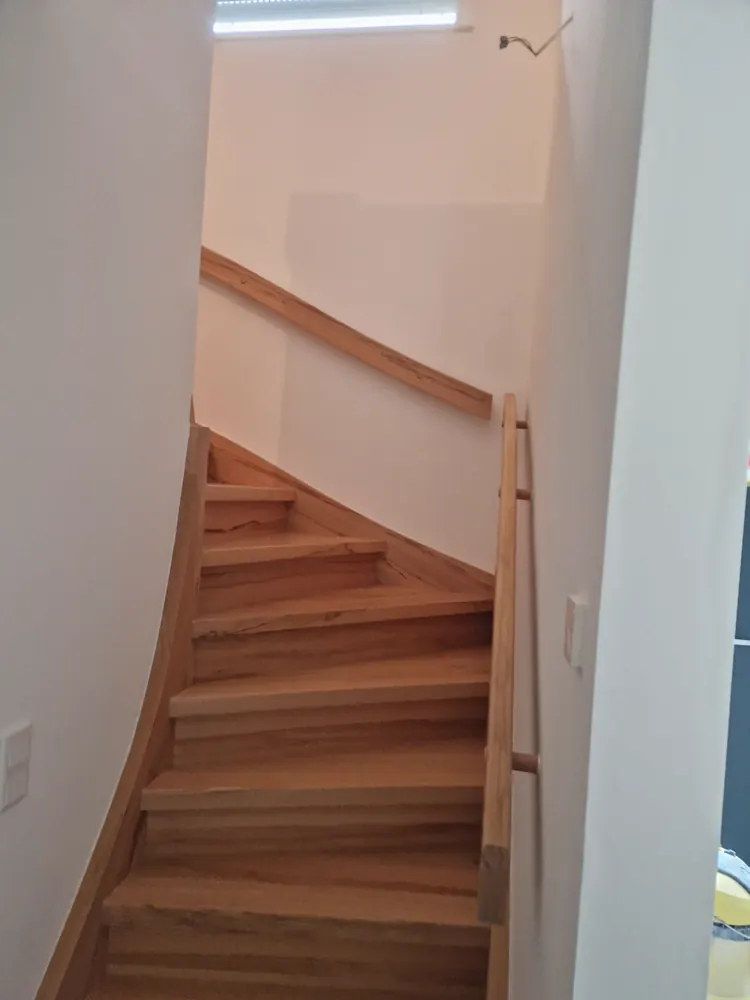 Neue Holztreppe mit hellen Stufen zwischen weiß gestrichenen Wänden