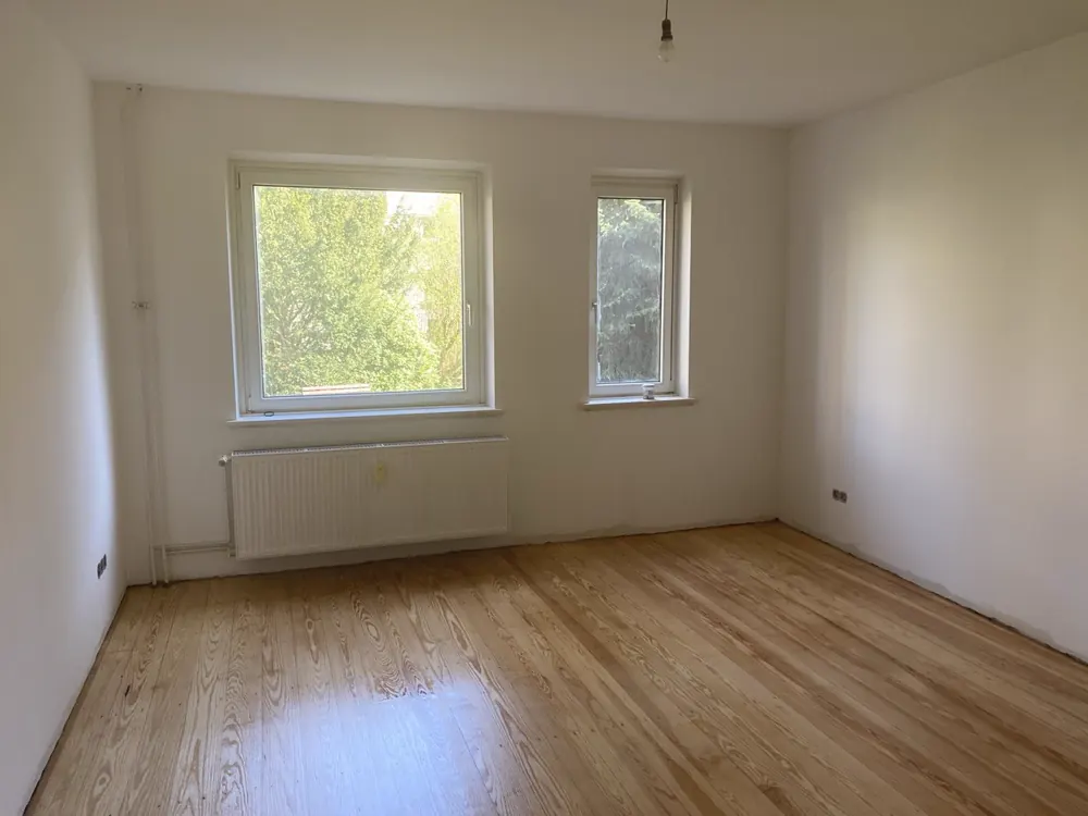 Fertig saniertes Zimmer mit neuem Parkett, weißen Wänden und zwei Fenstern